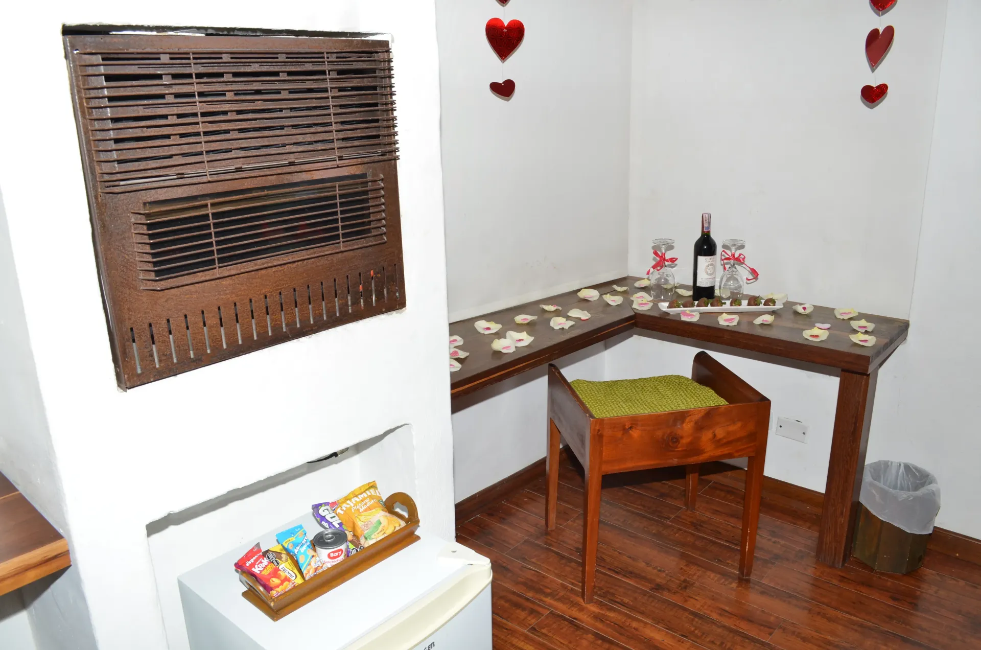 Un rincón de la habitación con un escritorio de madera decorado con pétalos, una botella de vino y una parrilla.