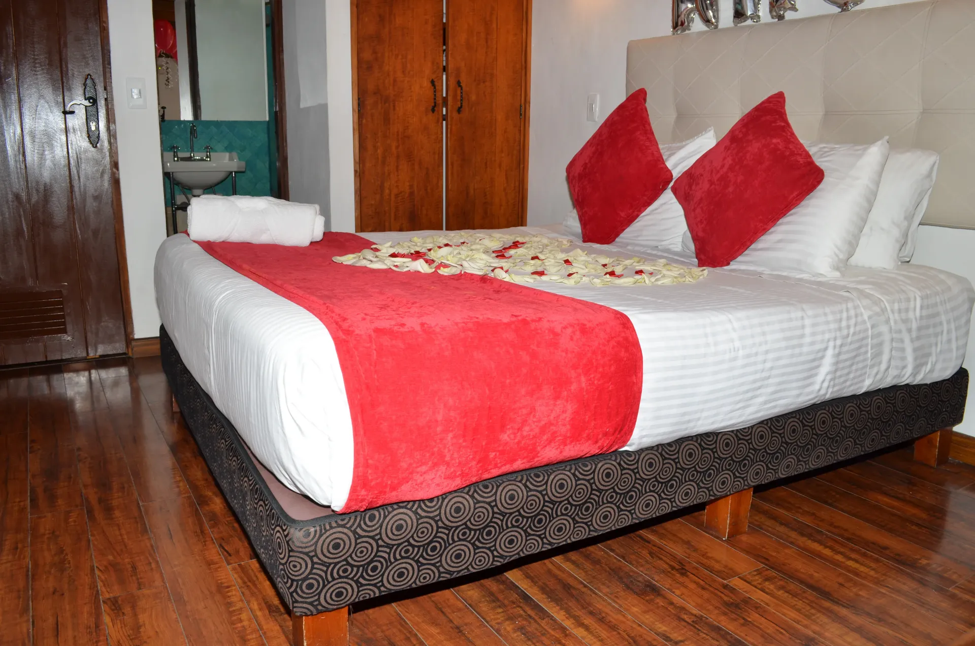 Dormitorio con cama blanca, almohadas rojas, flores y suelo de madera.
