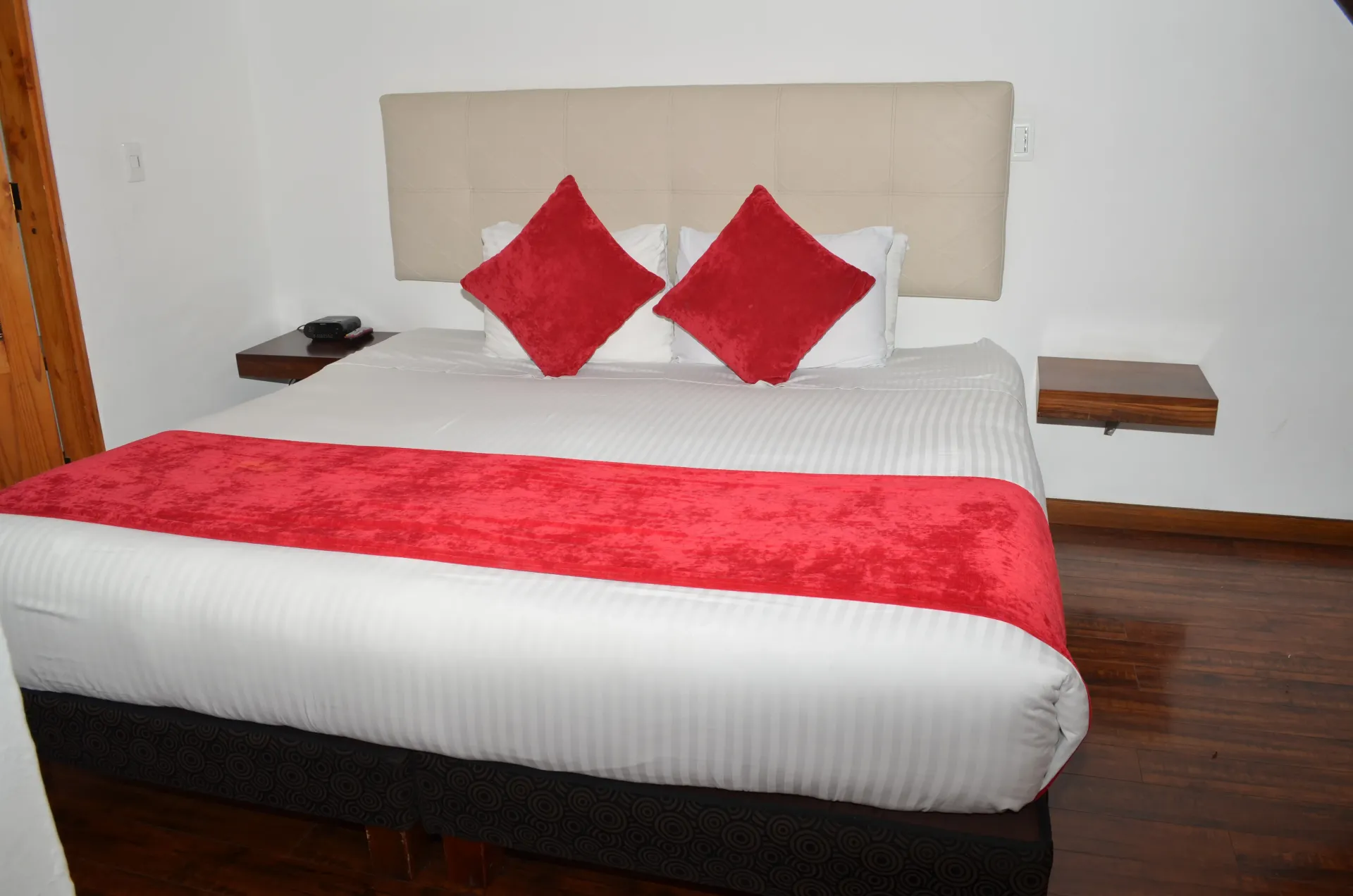 Una cama de hotel con edredón blanco y almohadas y manta rojas.