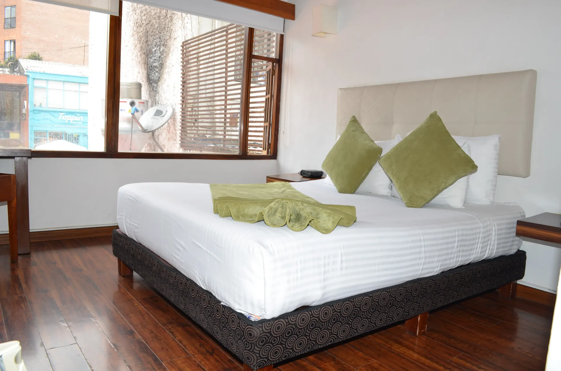 Dormitorio con cama, almohadas y suelo de madera. Ventana con vistas parciales.