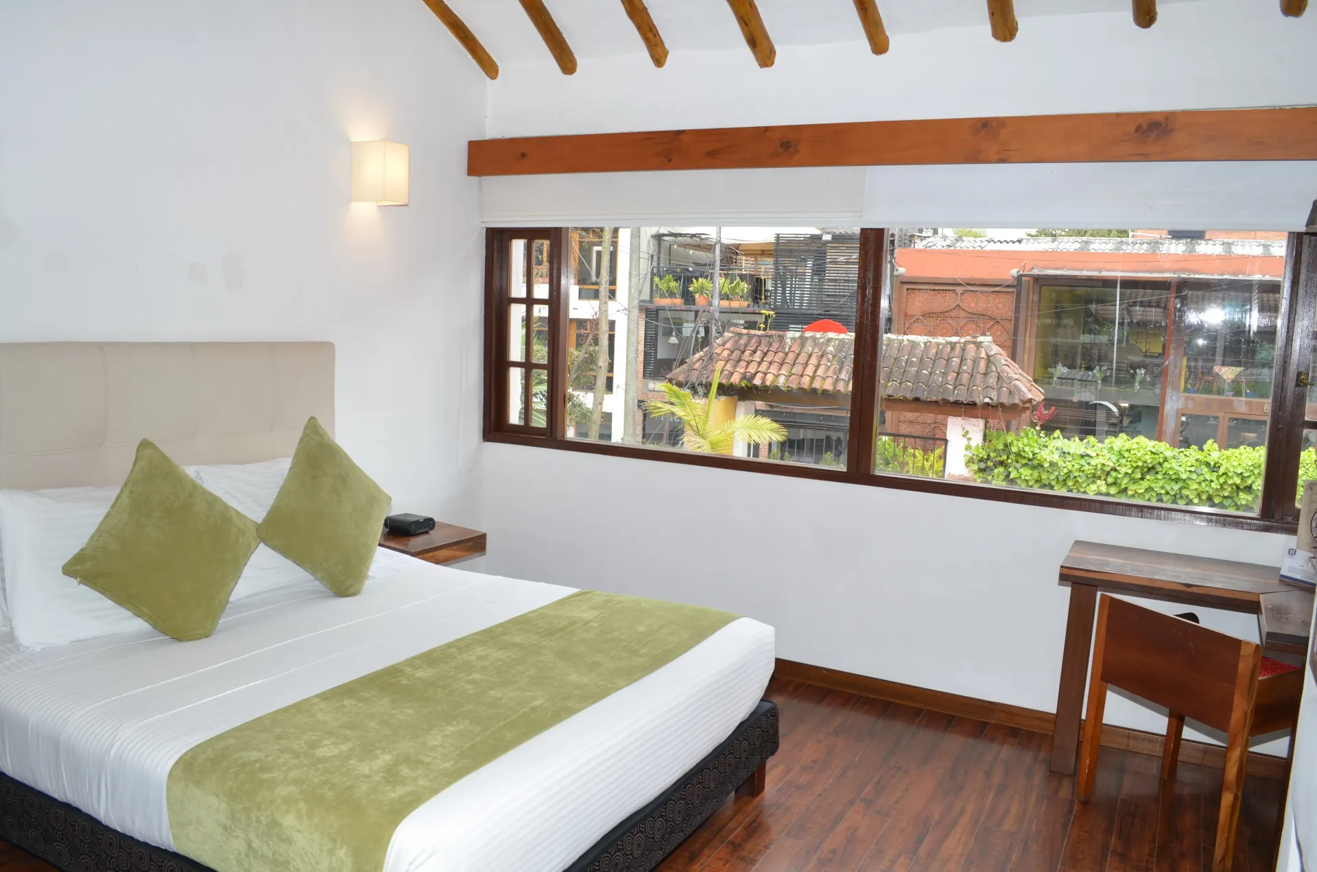 Habitación de hotel con cama, ventana con vistas a los edificios y detalles de madera.