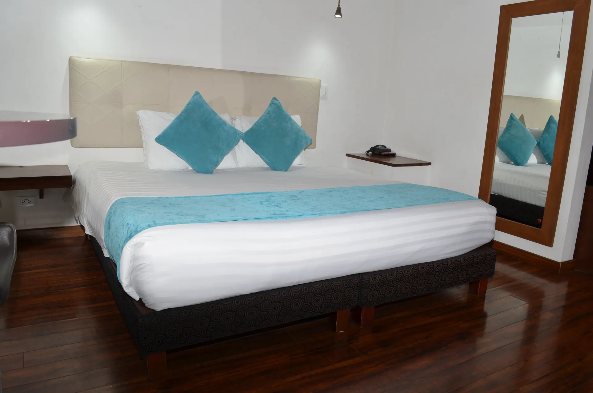 Dormitorio con cama, almohadas y alfombra azules, espejo grande y suelo de madera oscura.