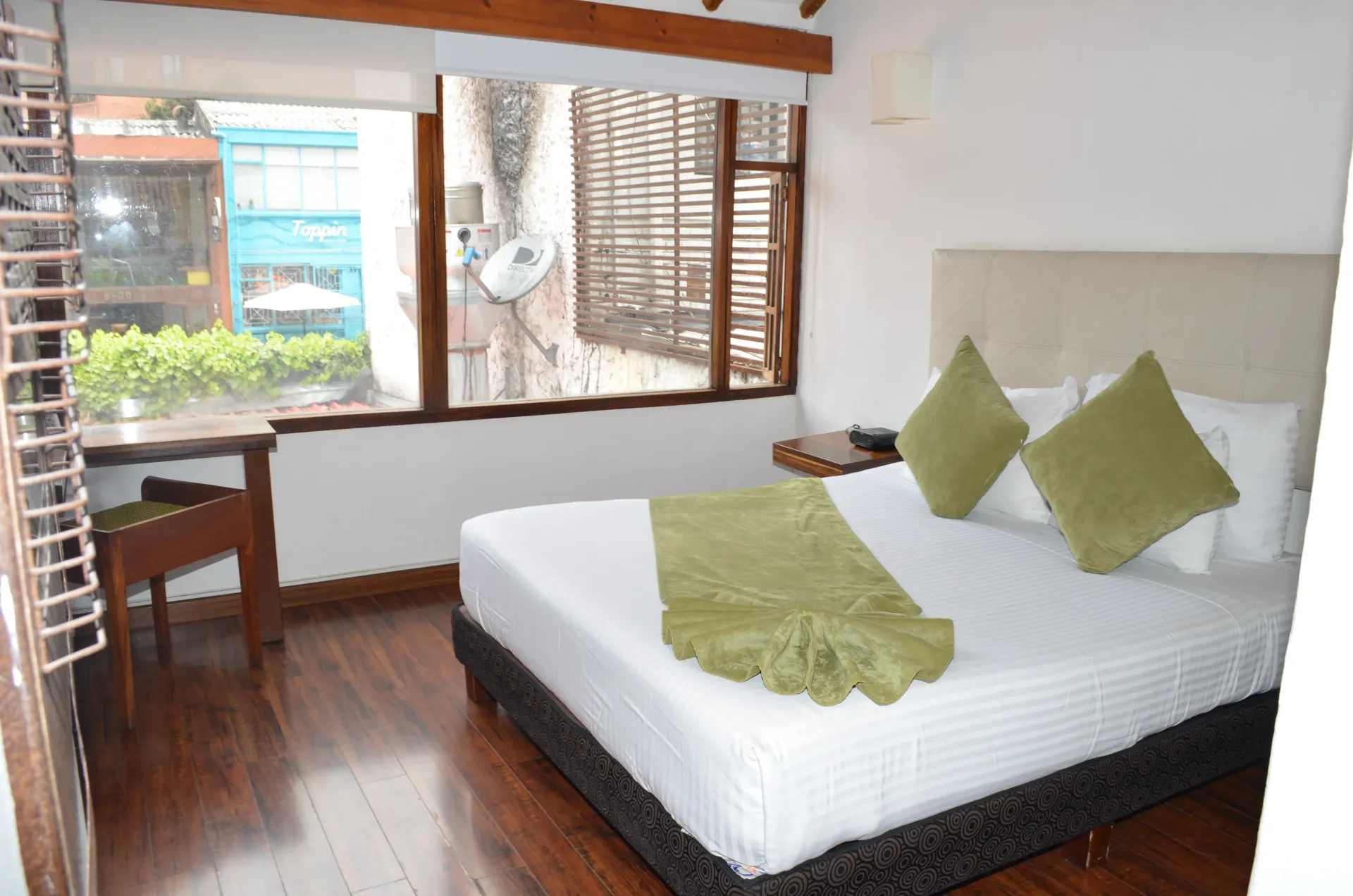 Habitación de hotel con cama, escritorio y ventana con vistas a la vegetación.