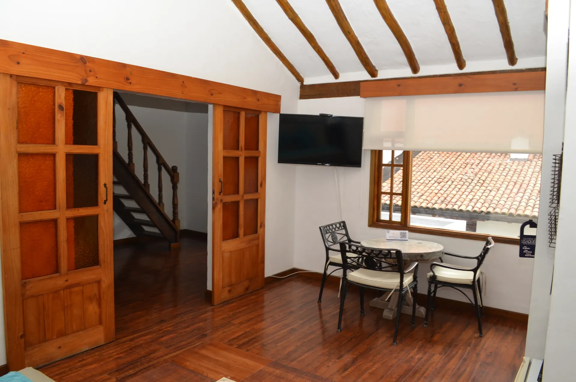 Habitación interior con suelo de madera, puertas correderas, escaleras, televisor, mesa y sillas.