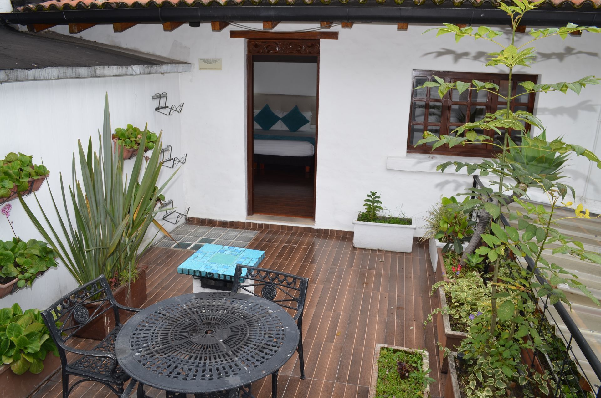 Patio con mesa, plantas y puerta que da a un dormitorio con almohadas en la cama.