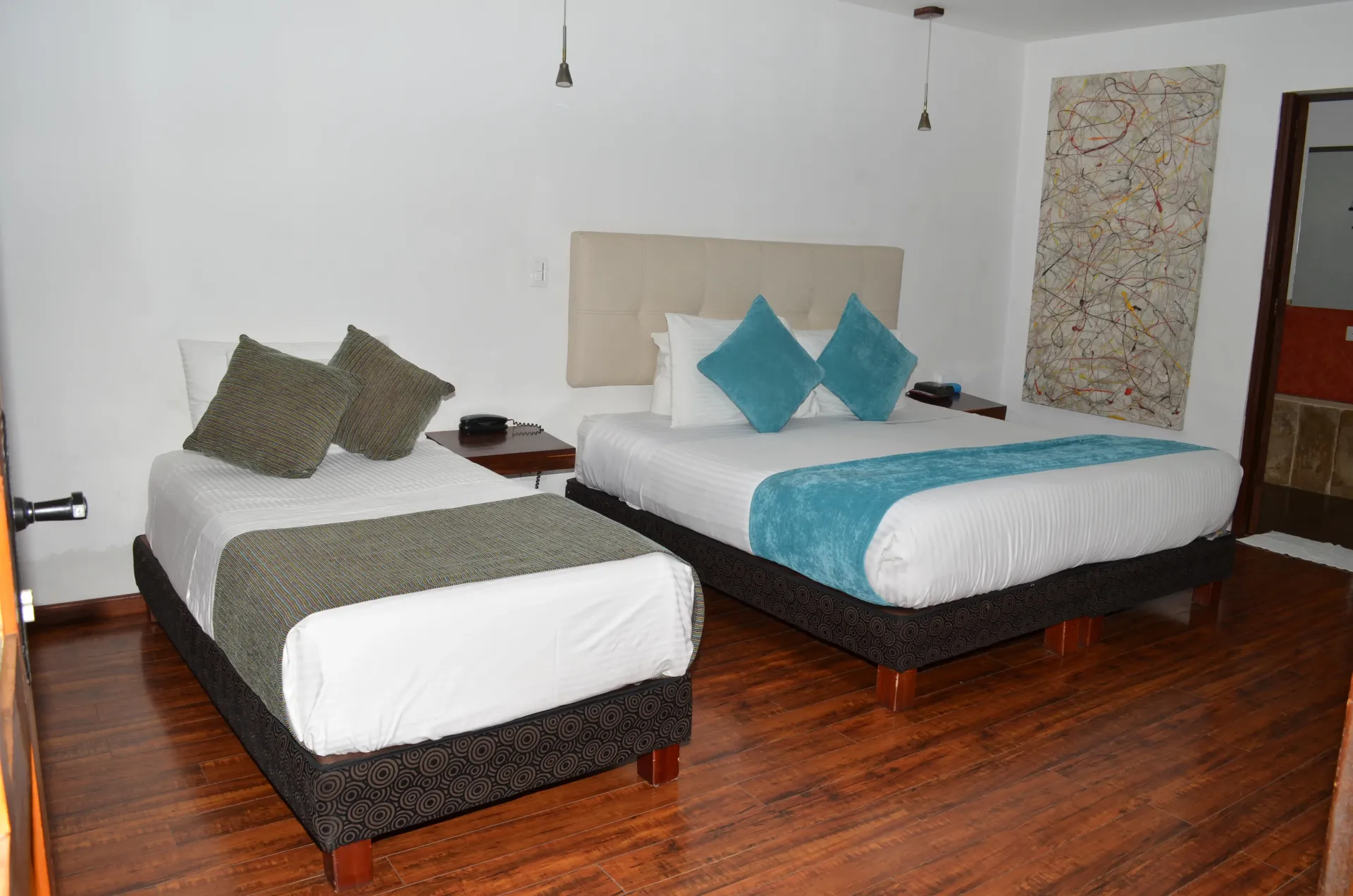 Habitación de hotel con dos camas, una doble y una individual, con sábanas blancas y almohadas decorativas.