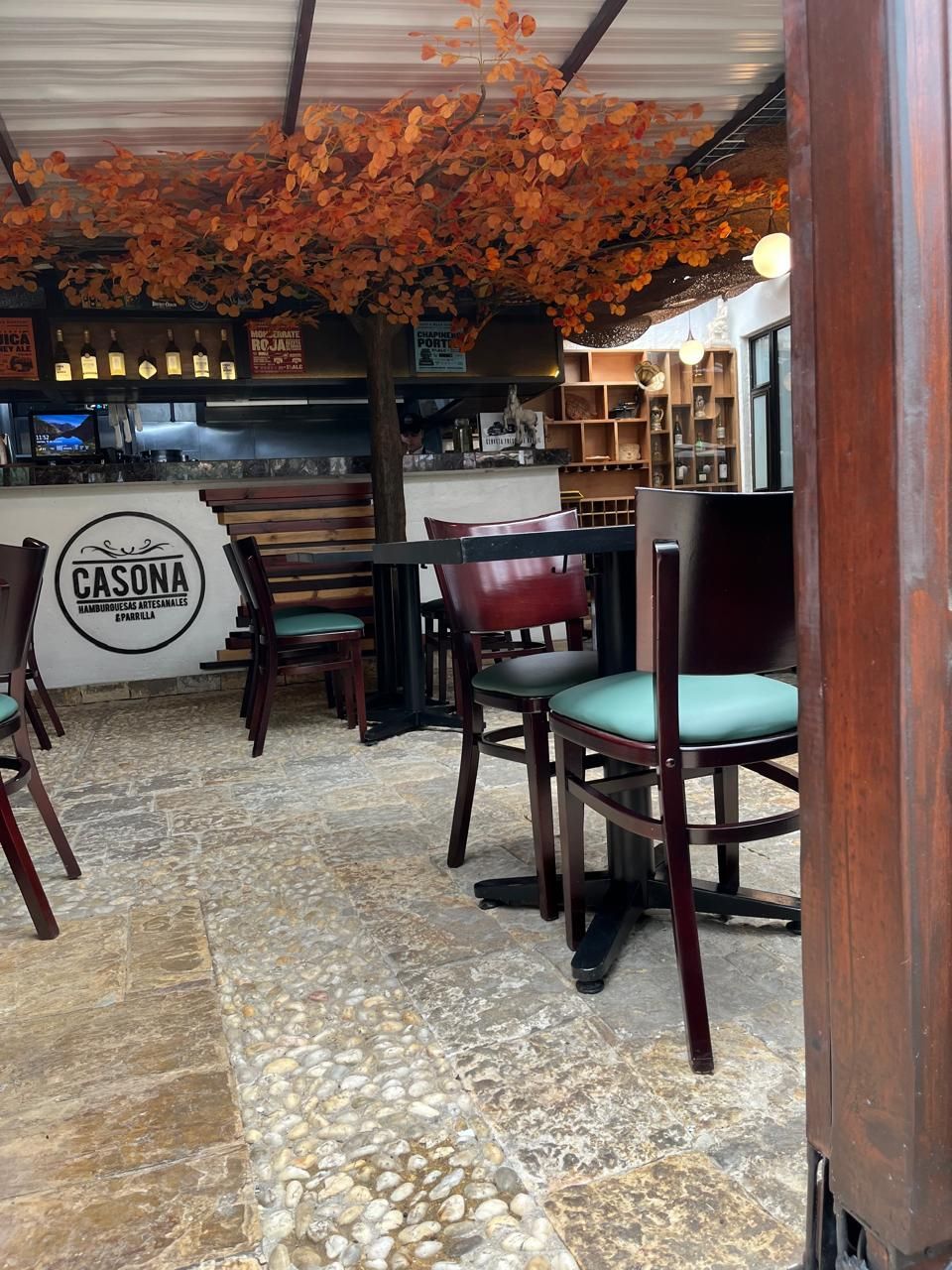 Terraza de cafetería; mesas y sillas bajo una pérgola de colores otoñales.
