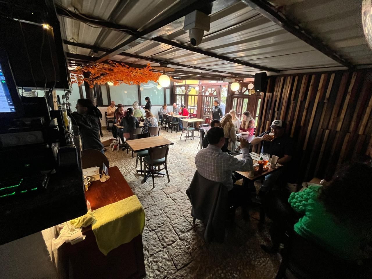 Interior de un restaurante con varias mesas y comensales. Algunos están sentados, otros de pie conversando.