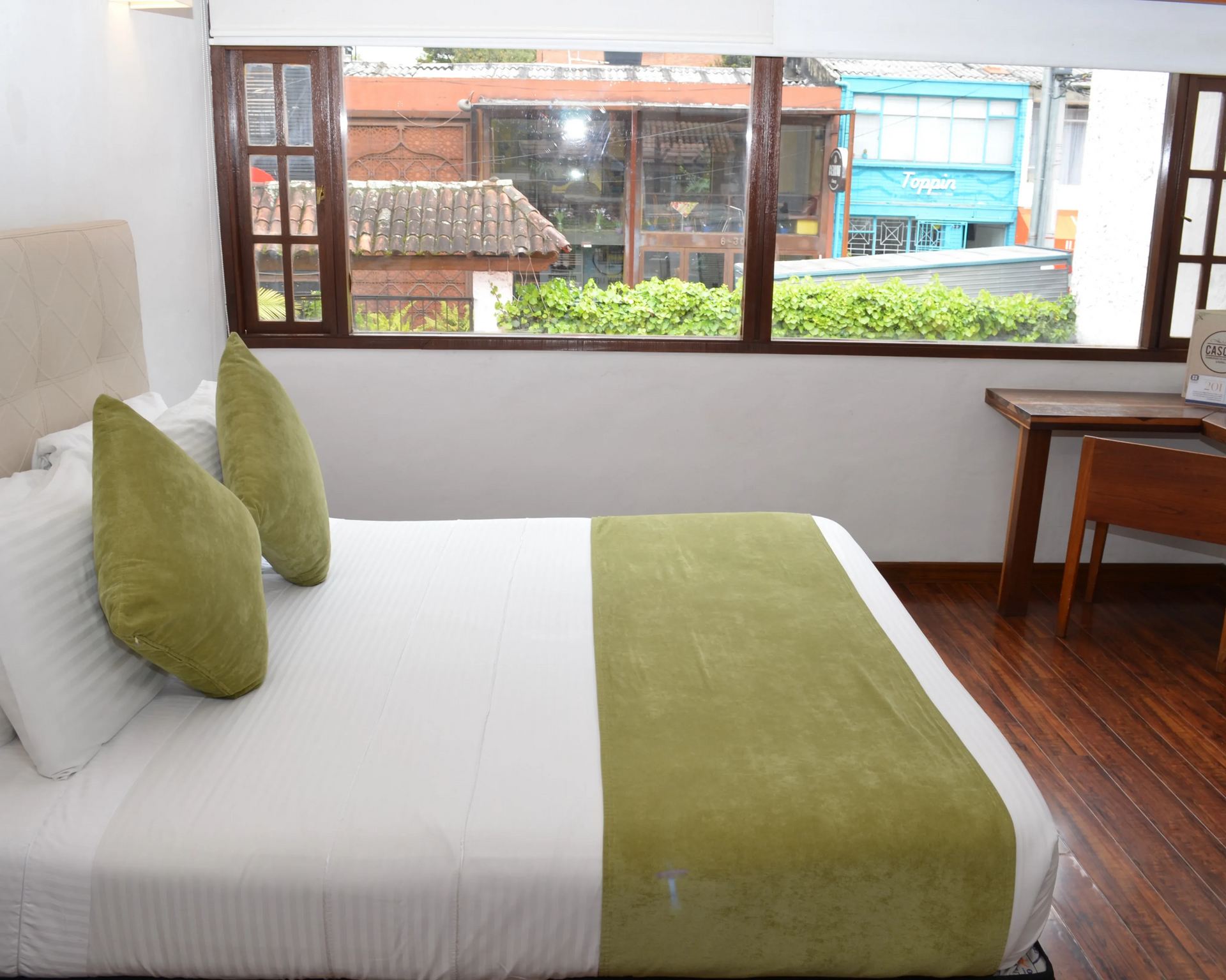 Habitación de hotel con cama, almohadas y ventana con vistas a la calle.