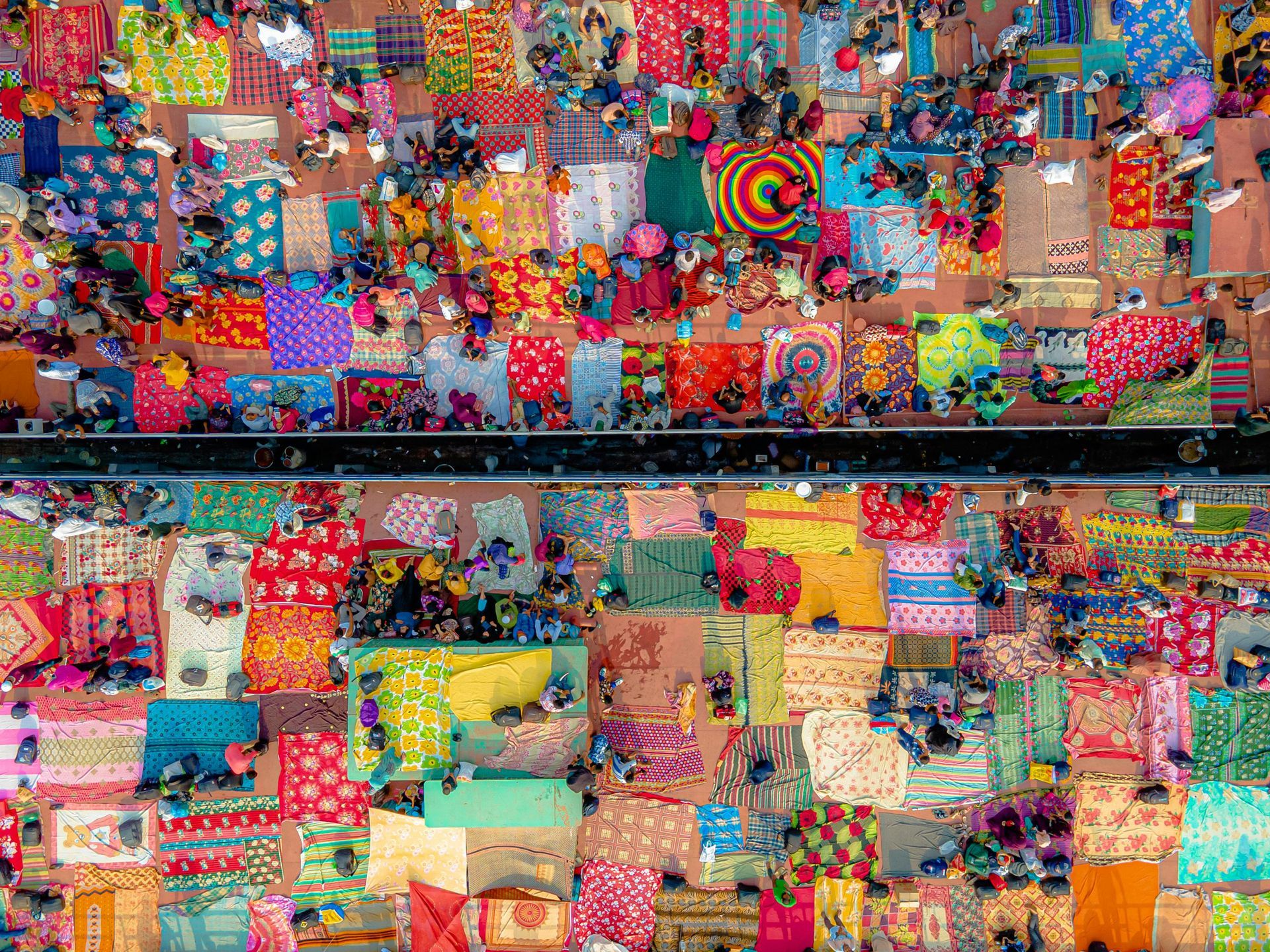 Overhead view of a bustling market with colorful textiles spread out and people milling about.