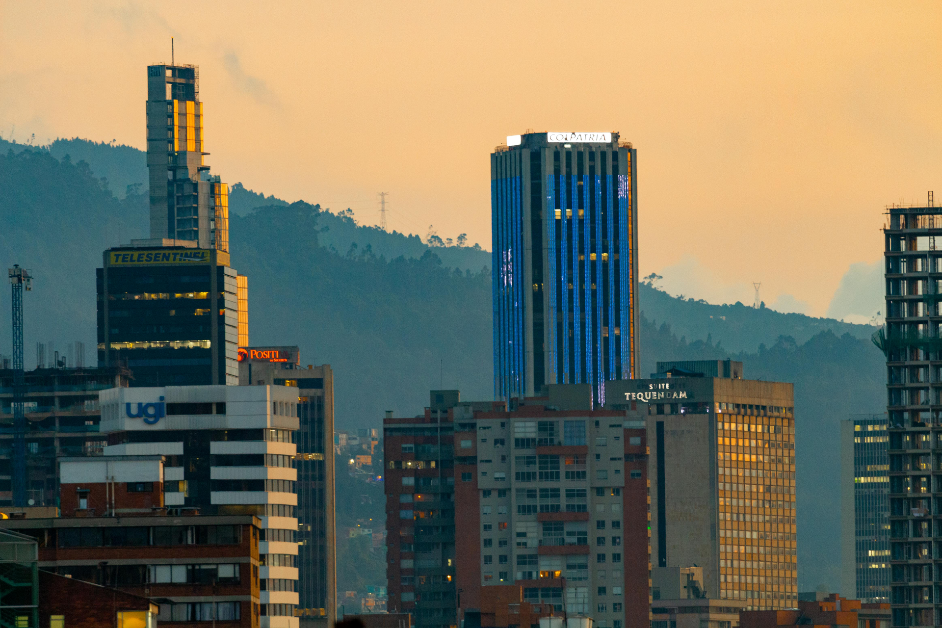 Horizonte de Bogotá, Colombia. Rascacielos con ventanas azules y doradas al atardecer, colinas verdes al fondo.