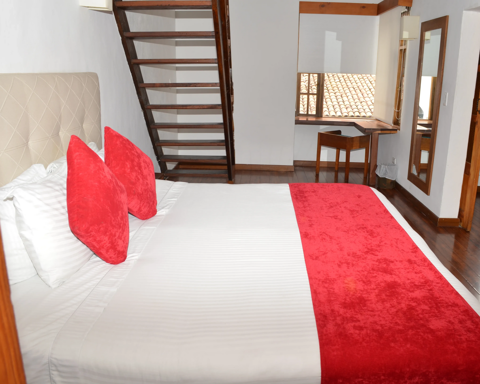 Dormitorio con cama, almohadas rojas y pie de cama, escalera de madera y escritorio.