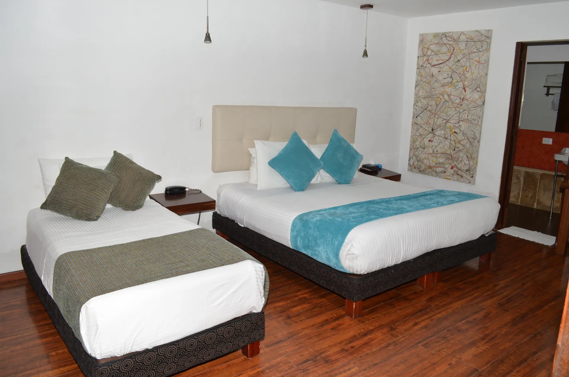 Habitación de hotel con dos camas: una doble y una individual, con detalles en verde azulado y gris.