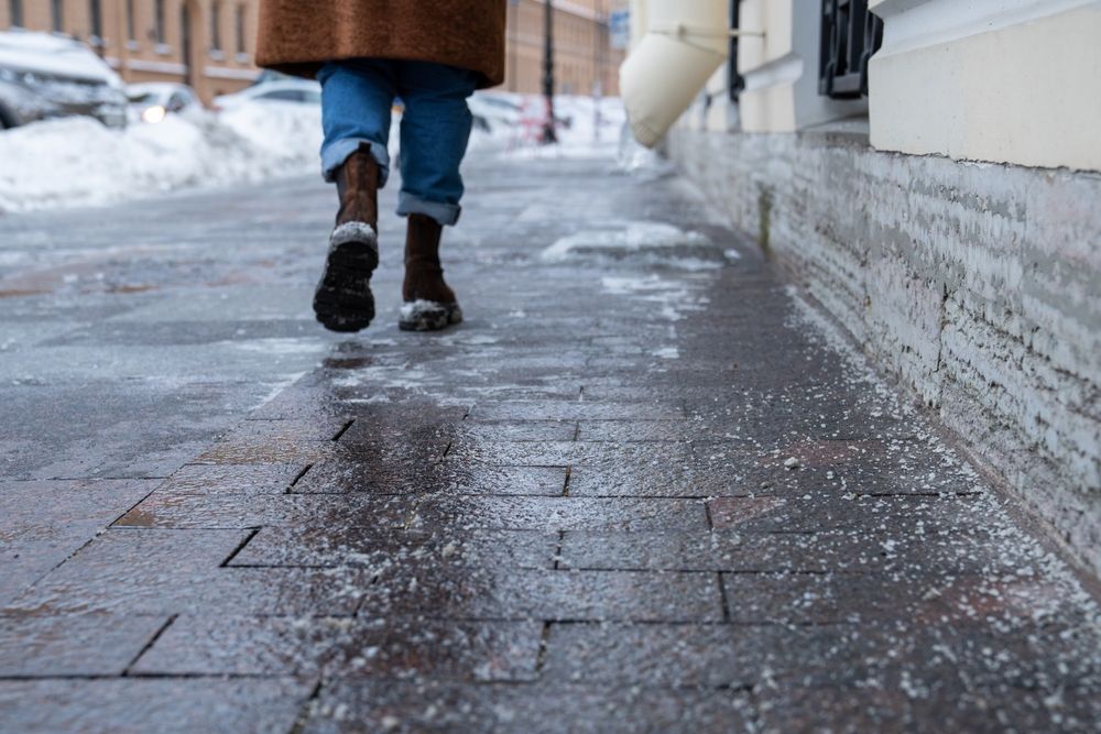 A person is walking on a wet sidewalk in the snow.