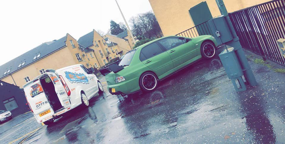 A green car undergoing a valeting service in a car park