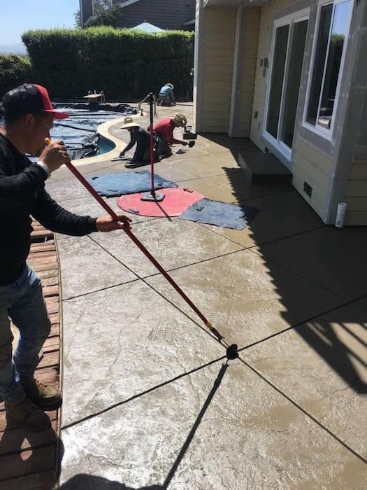 Two men are working on a concrete patio in front of a house