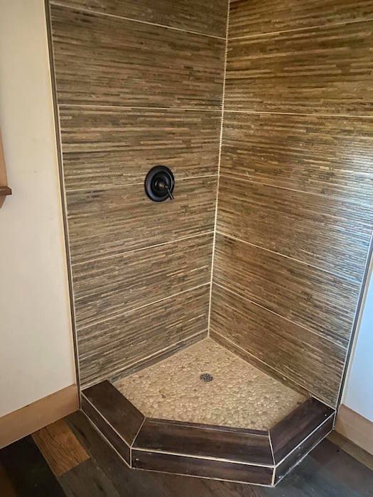 A shower stall with wooden tiles and a wooden floor in a bathroom.