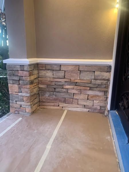 A brick wall is being painted on a porch.