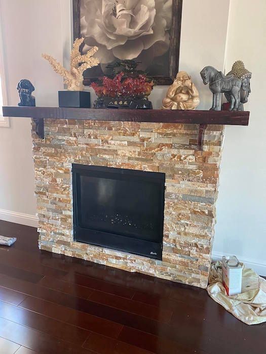 A living room with a stone fireplace and a wooden mantle.
