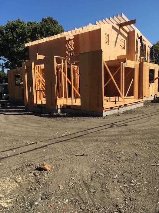 A wooden house is being built in a dirt lot