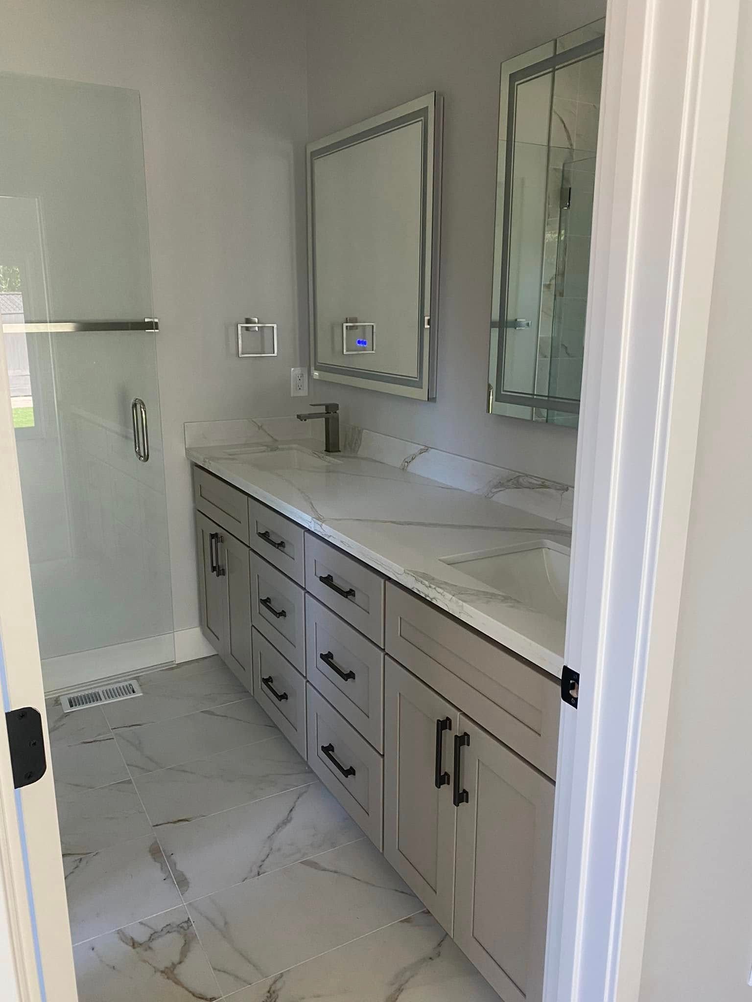 A bathroom with two sinks , two mirrors and a walk in shower.