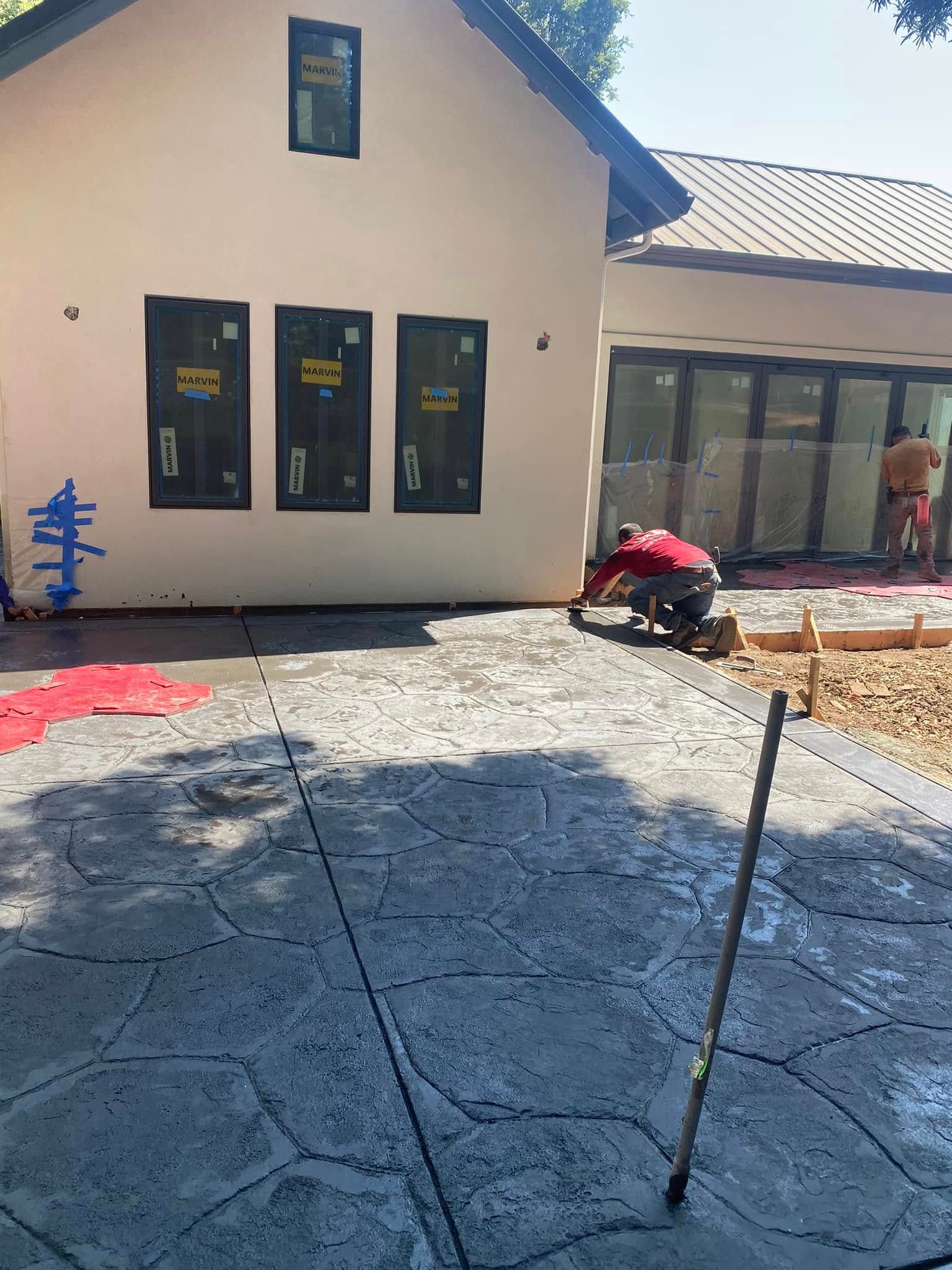 A man is working on a concrete patio in front of a house.