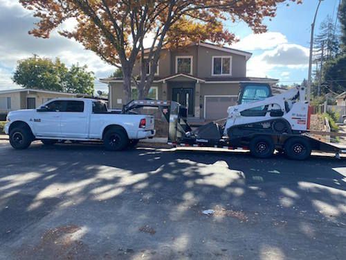 A white truck is towing a bobcat on a trailer.