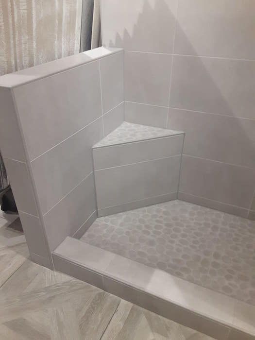 A shower stall with a corner seat in a bathroom.