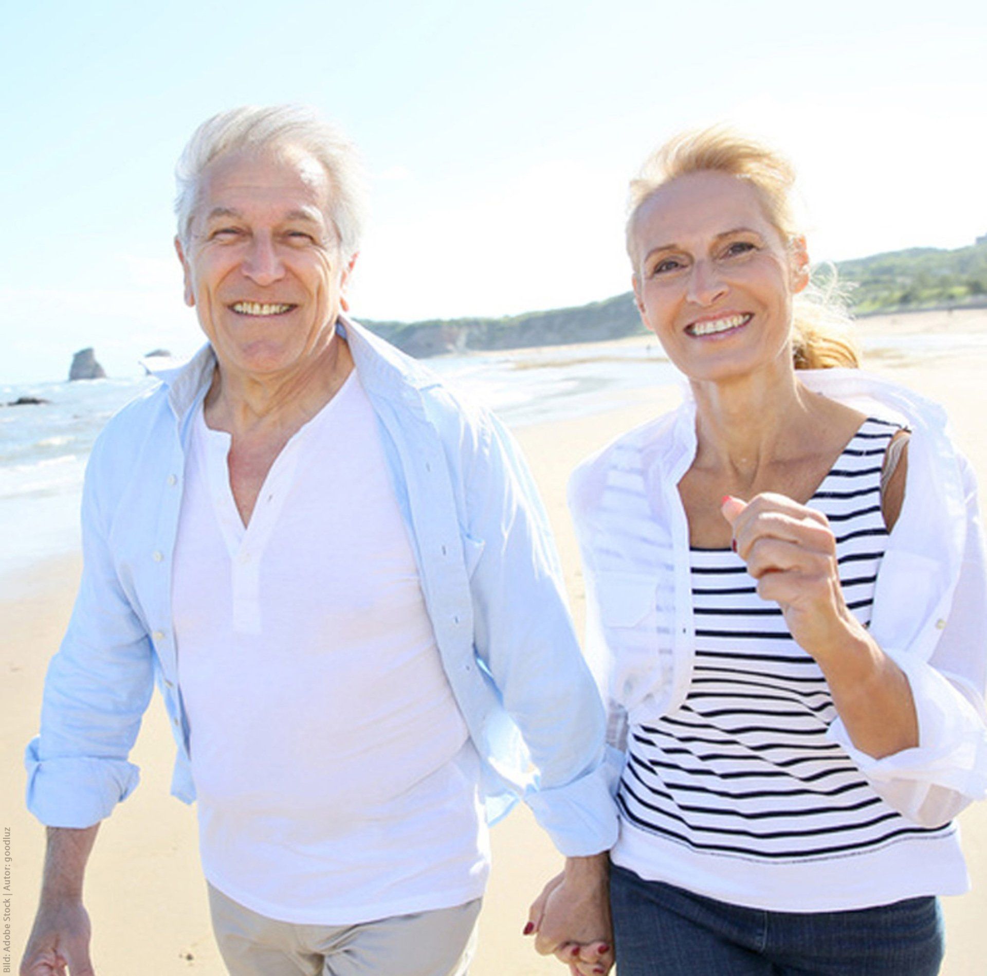 A man and a woman are walking on the beach holding hands and smiling.