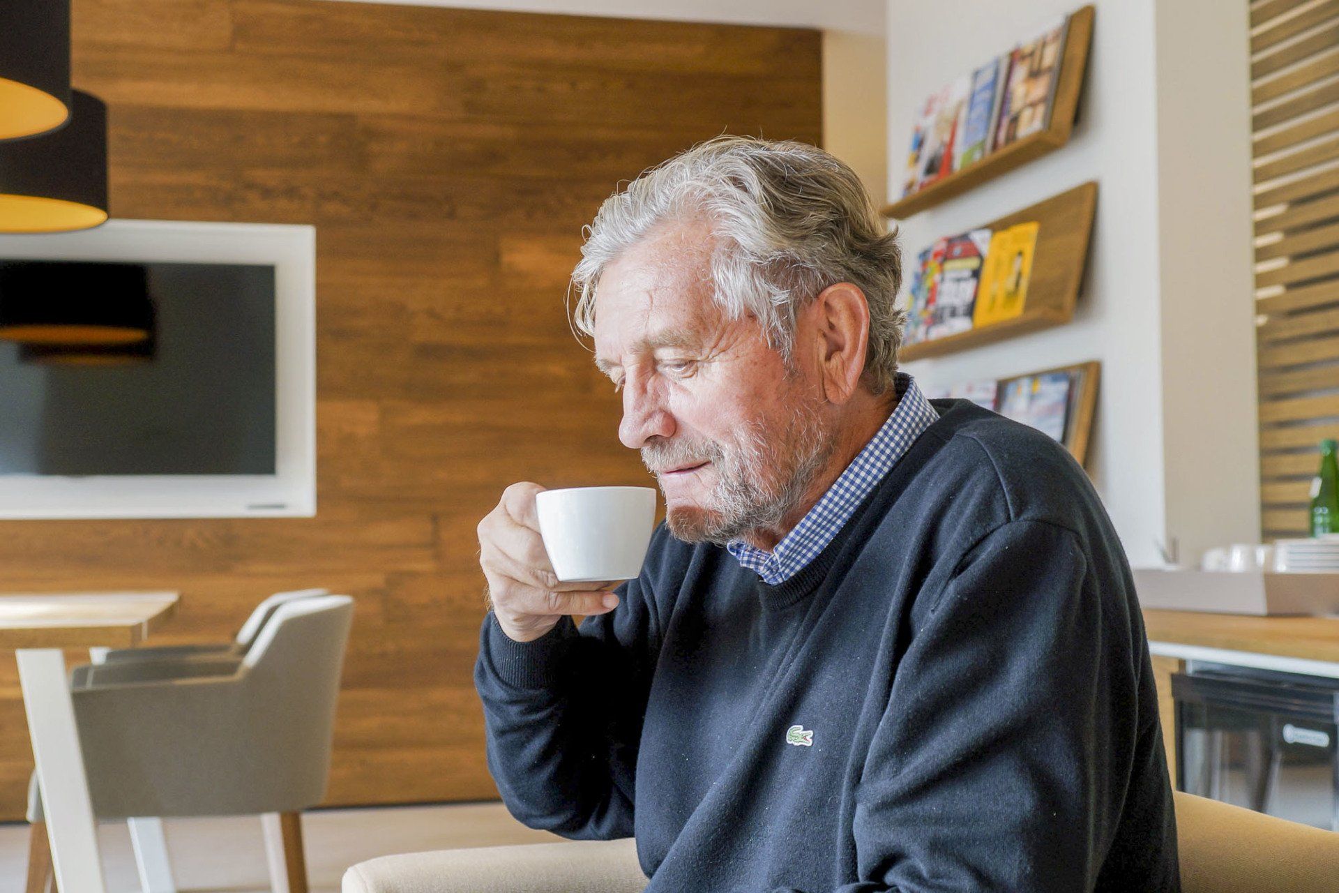 Ein älterer Mann sitzt auf einem Stuhl und trinkt eine Tasse Kaffee.