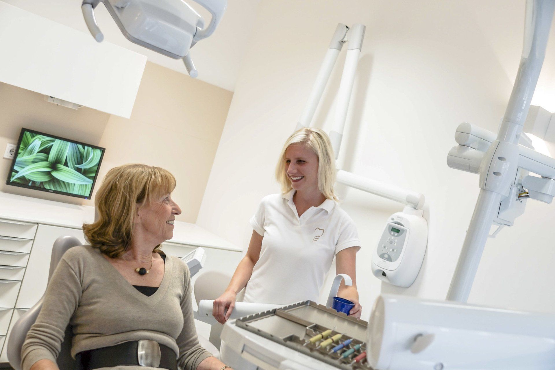 Eine Frau sitzt auf einem Zahnarztstuhl und unterhält sich mit einer Zahnärztin.