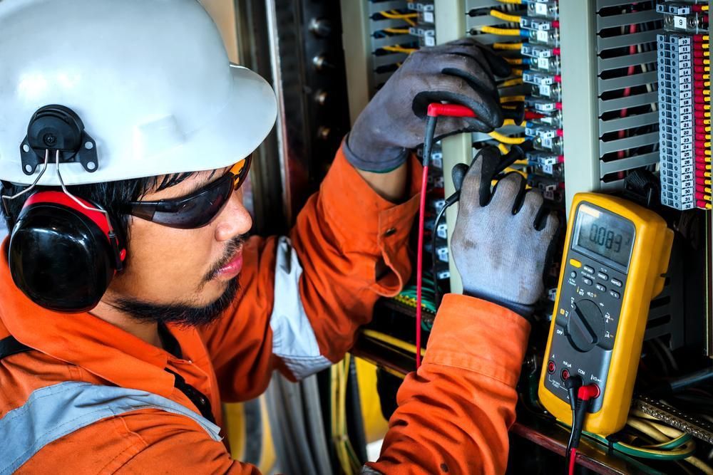 A Man Wearing Headphones and a Hard Hat is Working on an Electrical Box — Power & Data Support Services In Mareeba, QLD