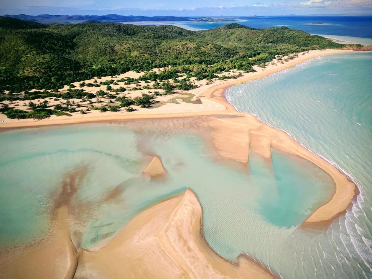 An Aerial View of a Sandy Beach Surrounded by Water and Mountains — Power & Data Support Services In Torres Strait, QLD
