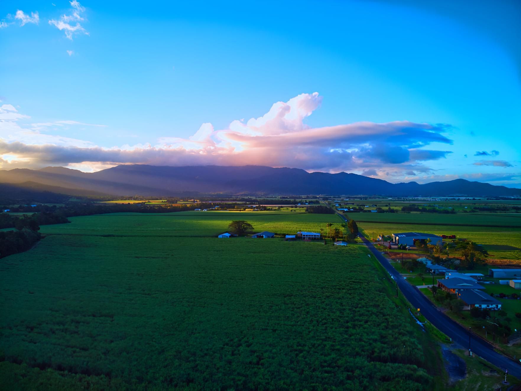 An Aerial View of a Lush Green Field With Mountains in the Background at Sunset — Power & Data Support Services In Tully, QLD