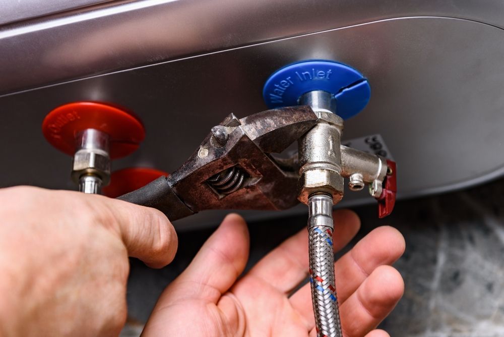 A person is fixing a water heater with a wrench.