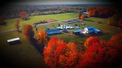 An aerial view of a farm surrounded by trees with autumn leaves.