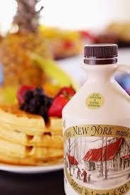 A bottle of new york maple syrup is sitting on a table next to a plate of waffles and fruit.