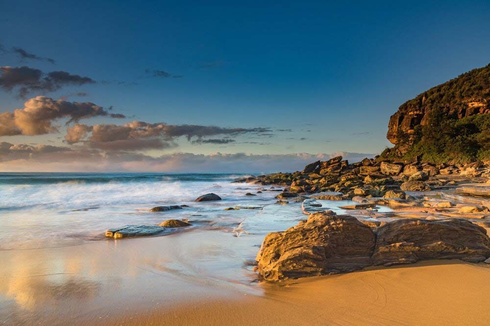 A Rocky Beach With Waves Crashing On The Shore At Sunset — Shop Fittings Office Furniture Materials Handling In Central Coast, NSW