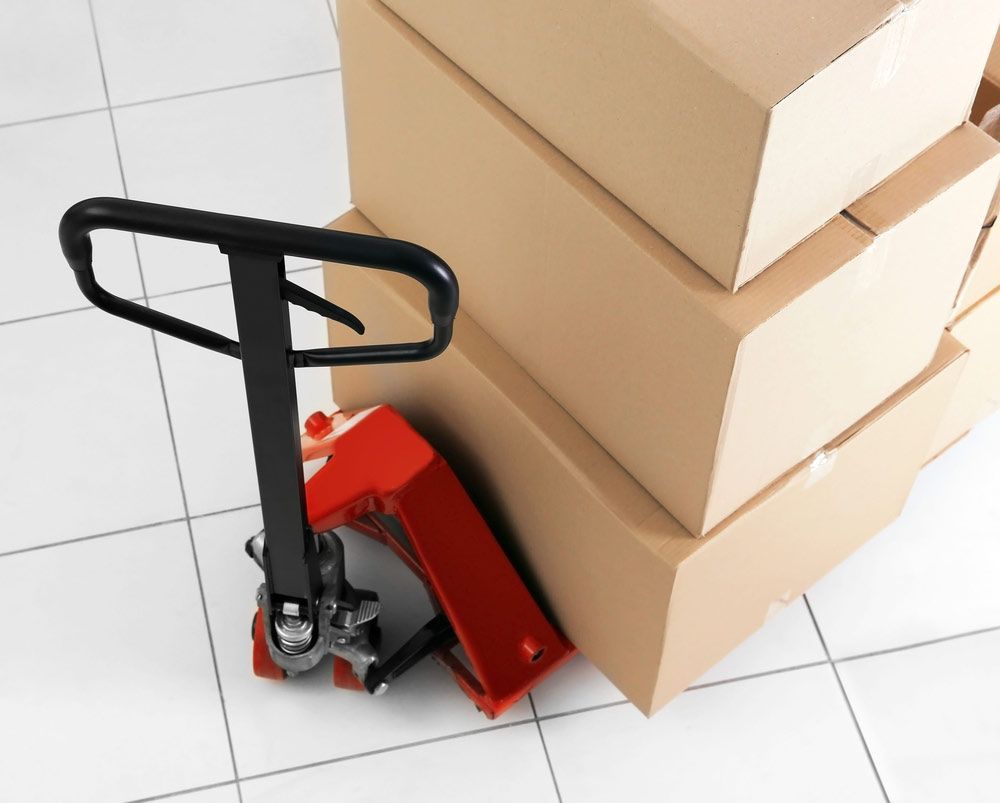 A Pallet Truck Is Sitting Next To A Stack Of Cardboard Boxes — Shop Fittings Office Furniture Materials Handling In Gosford, NSW