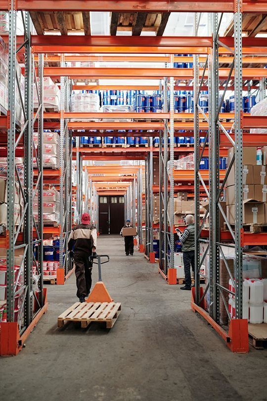 A Man Is Pushing A Pallet In A Warehouse — Shop Fittings Office Furniture Materials Handling In Gosford, NSW