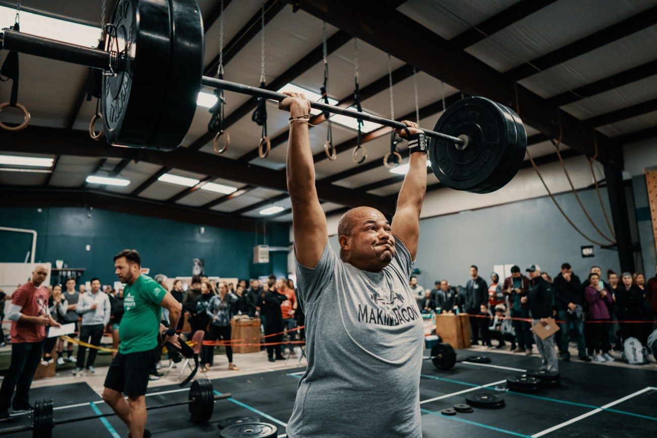 Man lifts a barbell overhead in a gym, with a crowd watching.