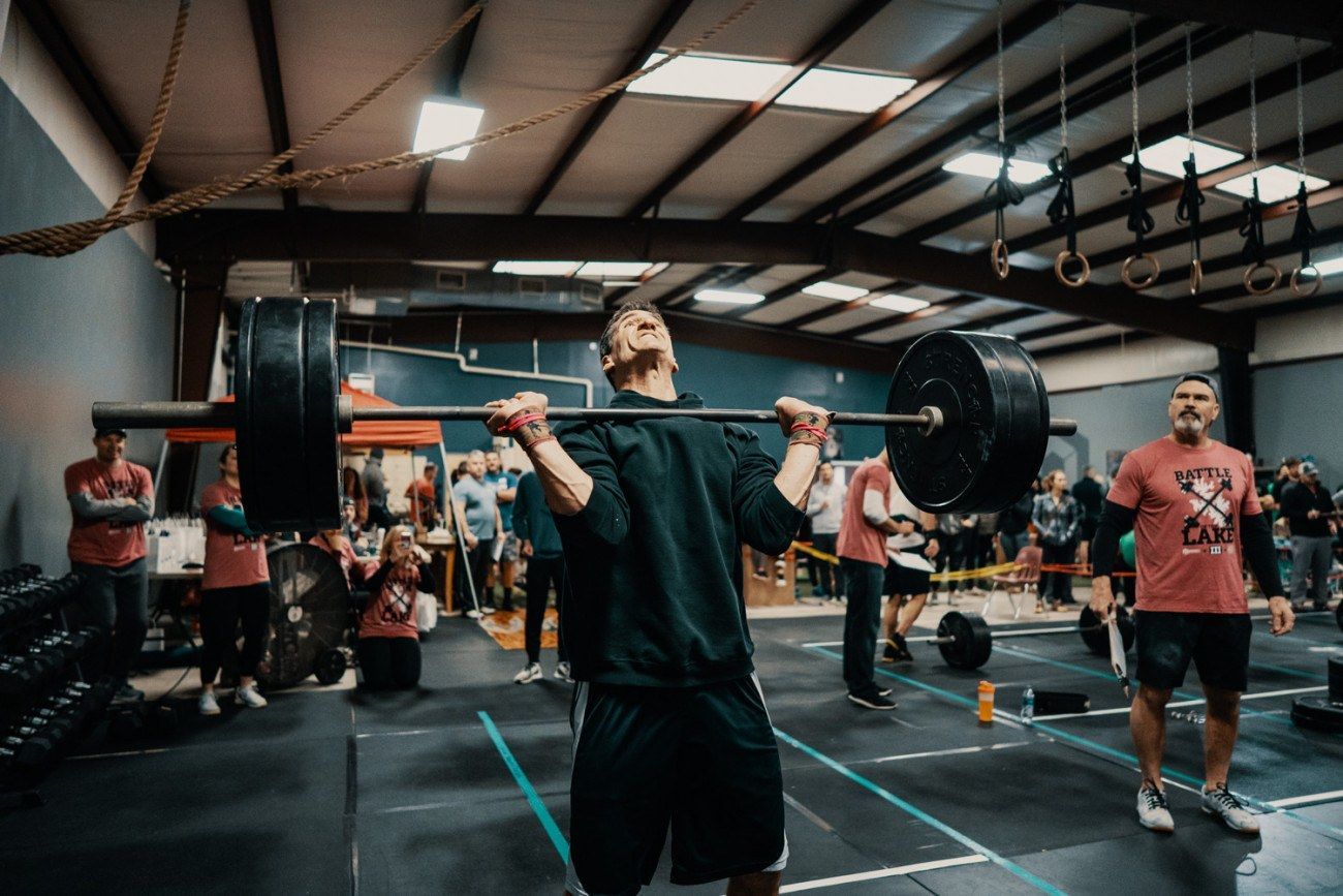 Man lifting a heavy barbell overhead in a gym, with onlookers.