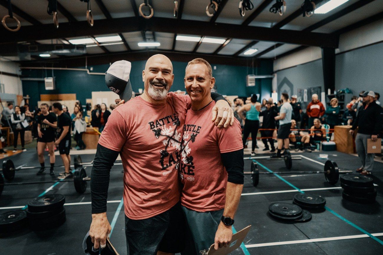 Two men in matching shirts with arms around each other at a CrossFit competition.