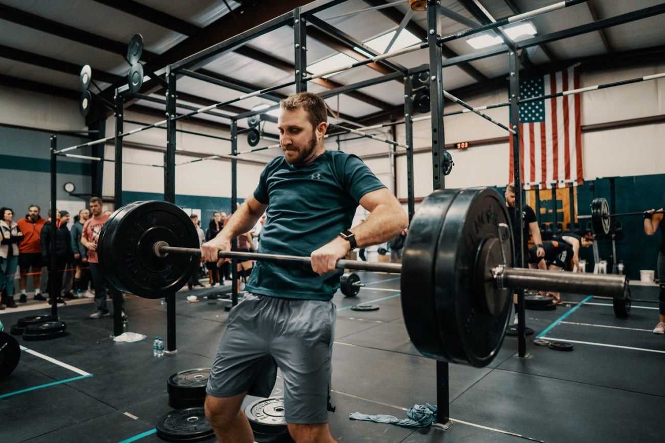 Man lifting a barbell in a gym, with crowd in background.