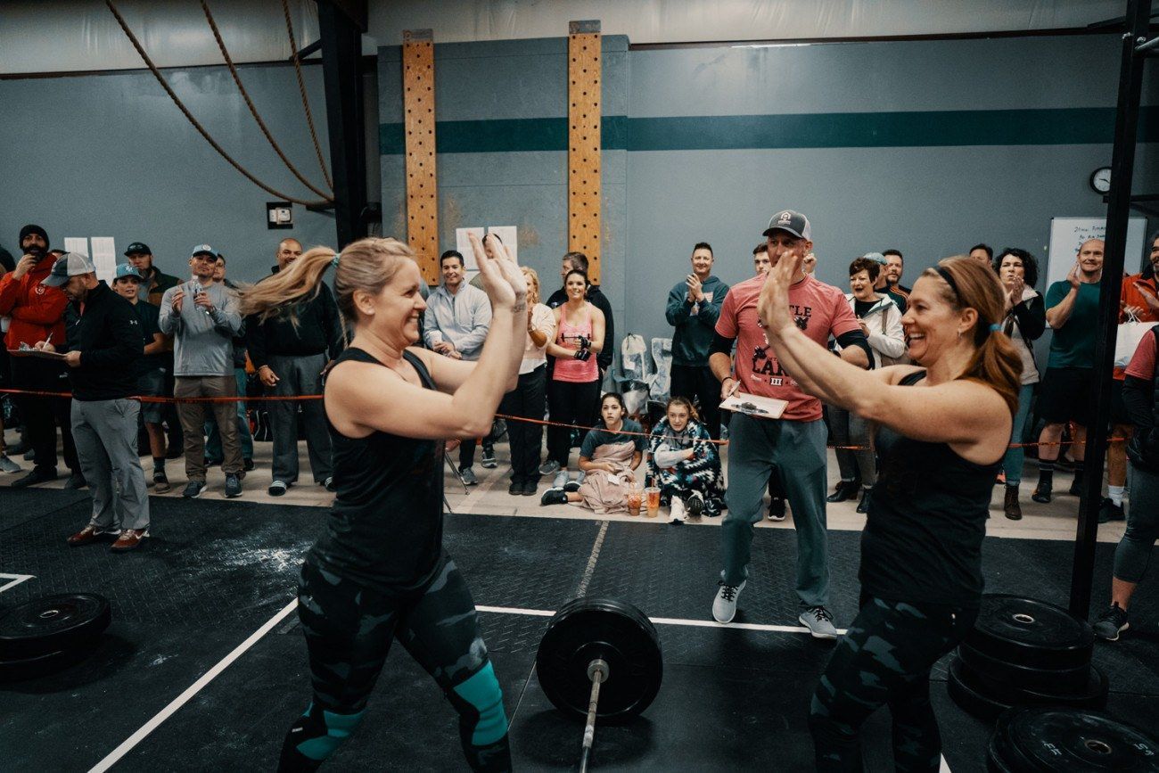 Two women high-five after lifting weights in a CrossFit gym. People clap in the background.