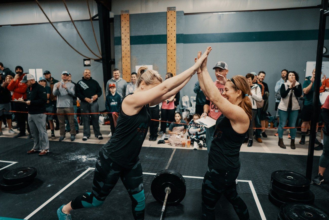 Two athletes high-five after a workout at a gym; crowd applauds.