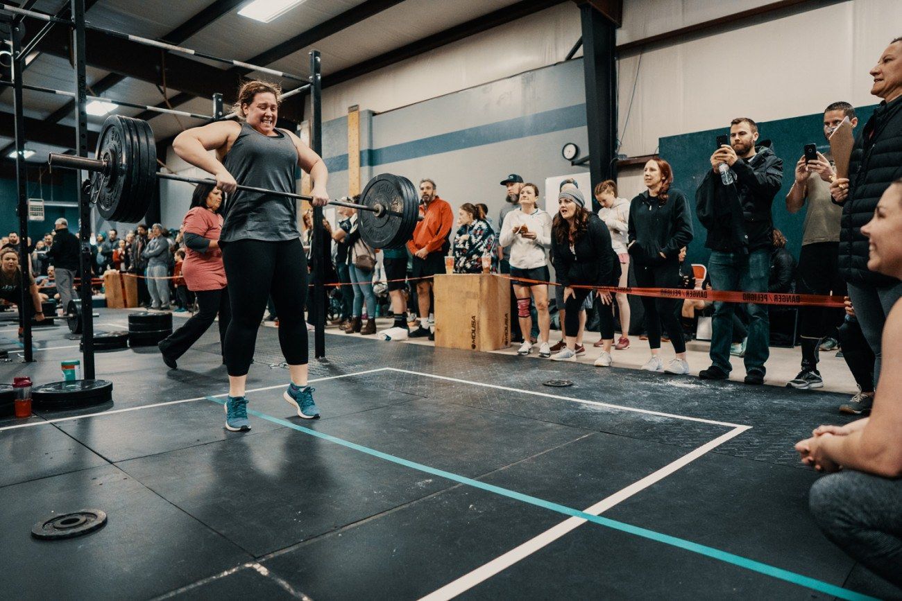 Woman lifting barbell in a gym, surrounded by spectators.