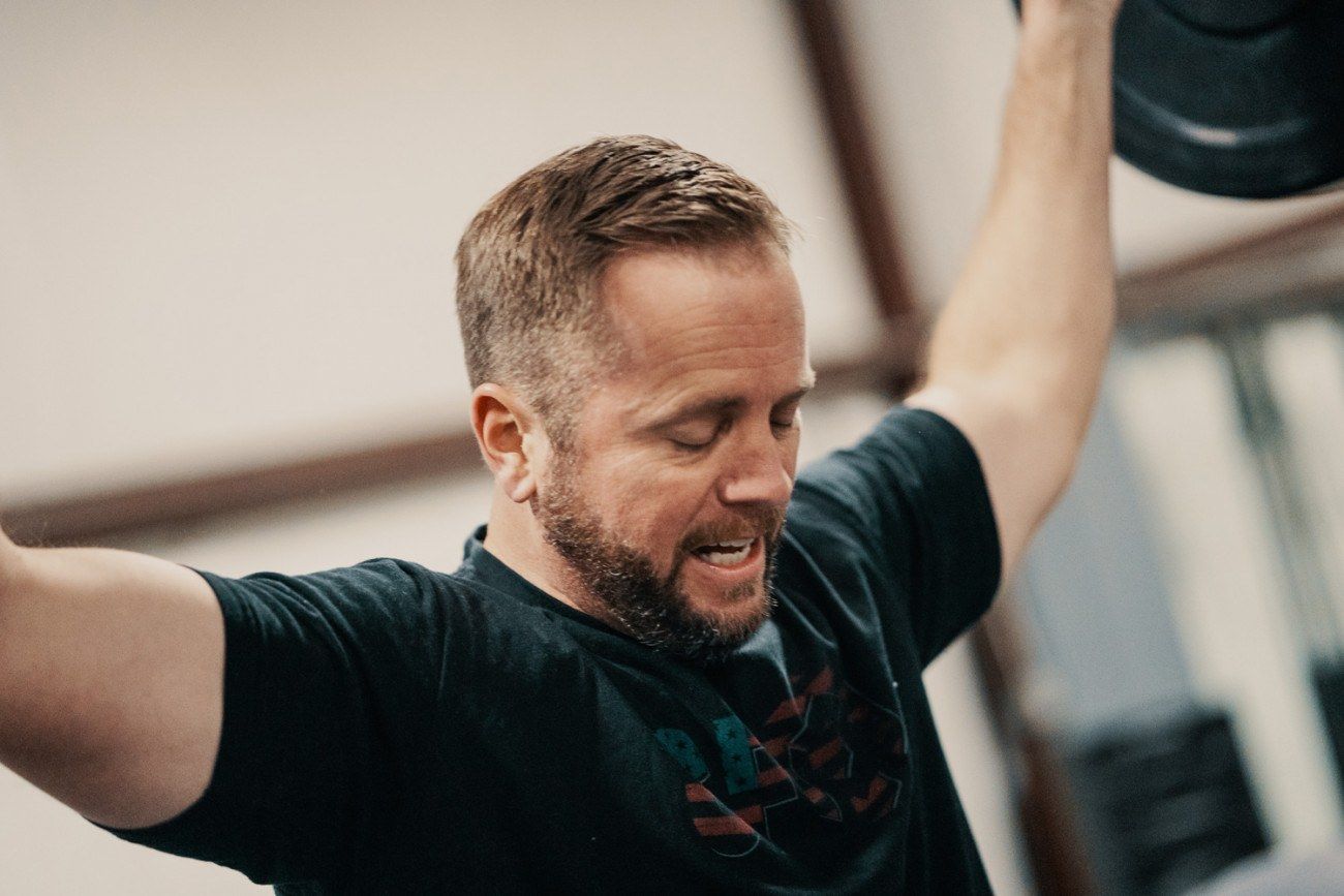 Man lifting weights overhead, eyes closed in concentration, in a gym.