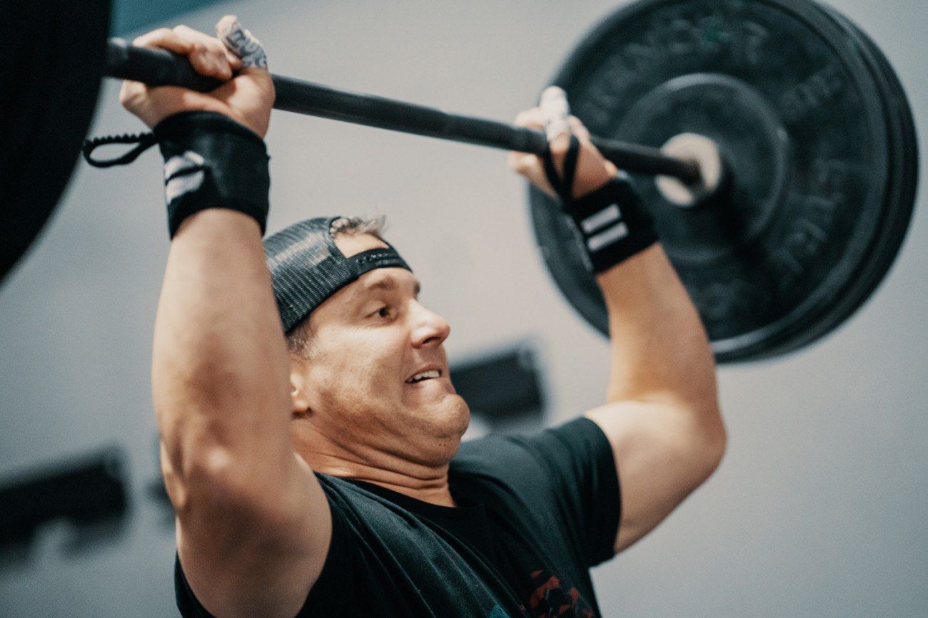 Man lifting a barbell overhead, straining with focused expression, in a gym.