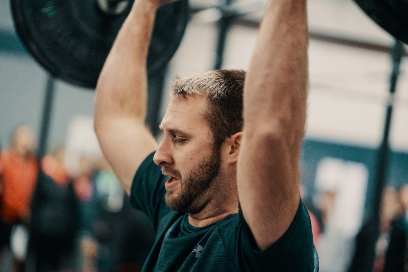 Man lifting barbell overhead in a gym, face strained, arms extended.